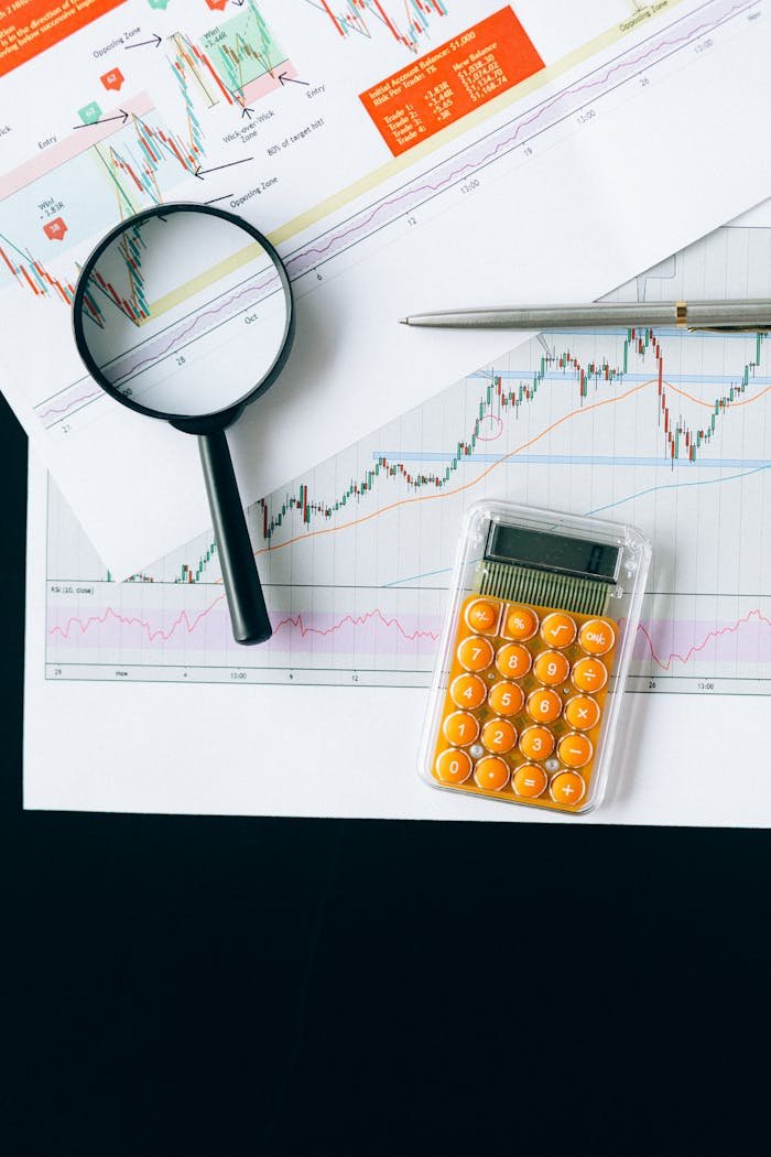 Close-up of financial documents with charts, calculator and magnifying glass for analysis.